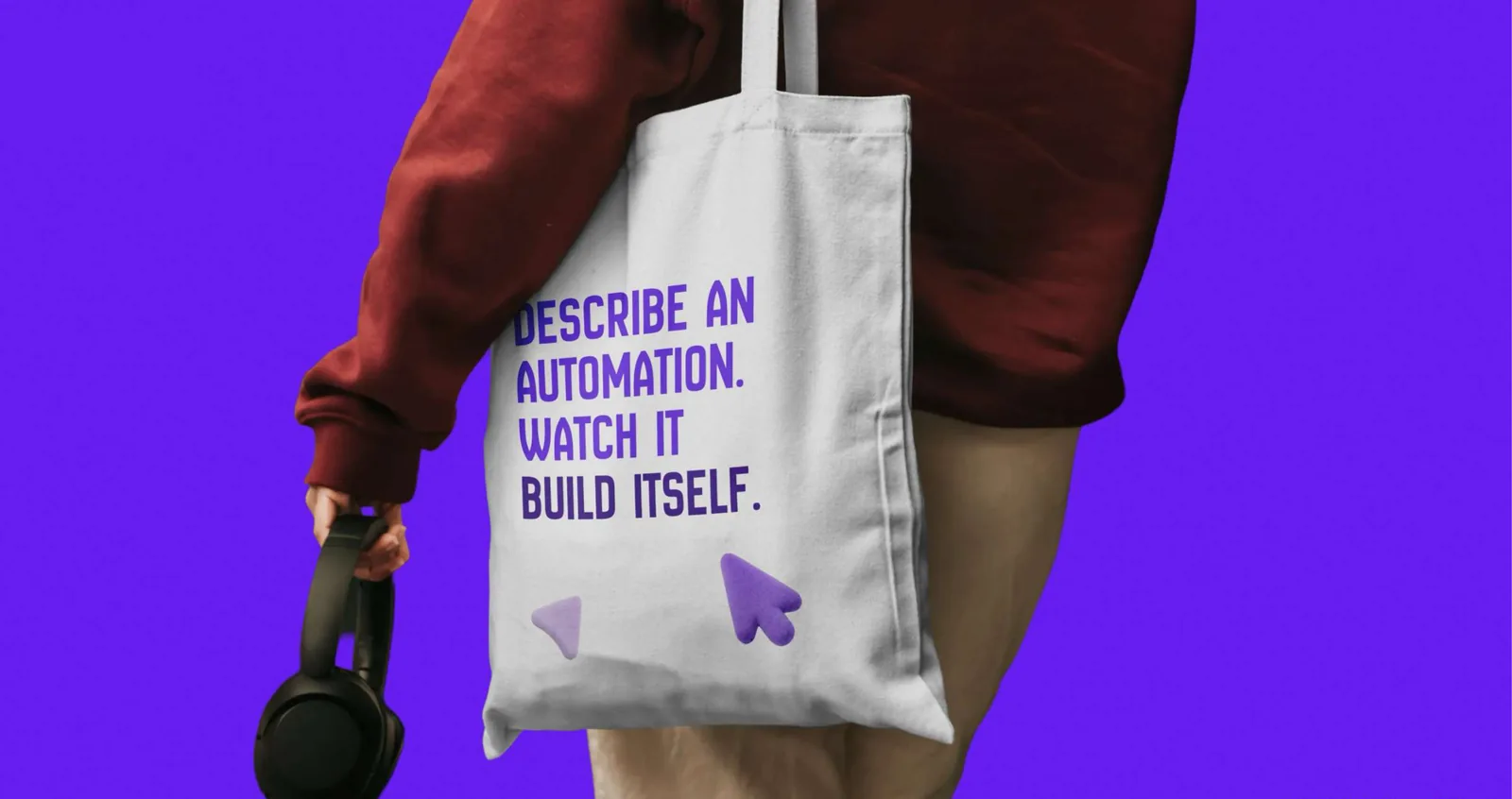 A canvas tote printed in Electric Indigo with “Describe an automation. Watch it build itself.” and two 3D cursors.